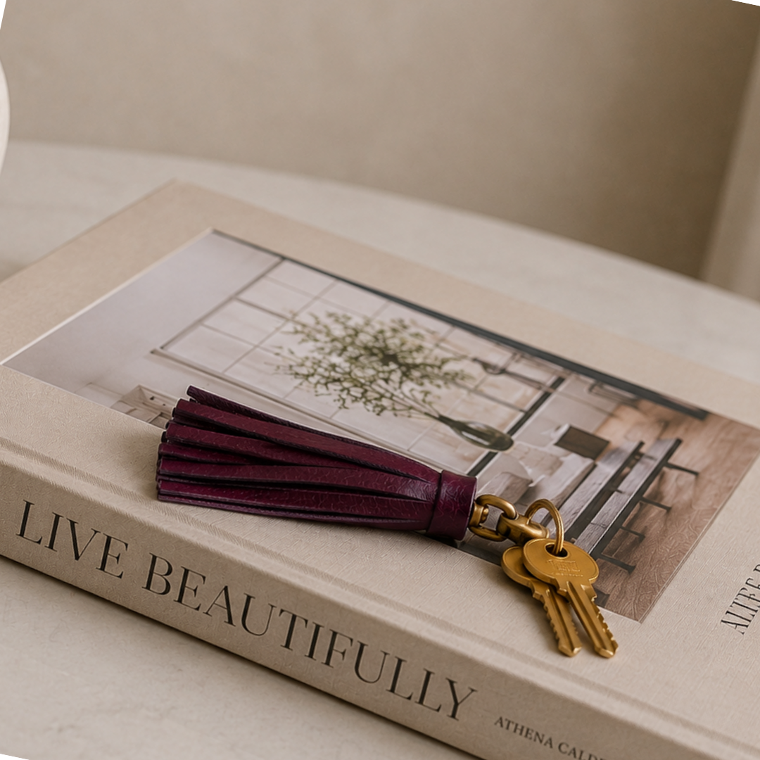 Llavero de cuero violeta con flecos y herraje vintage sobre libro decorativo beige estilo luxury