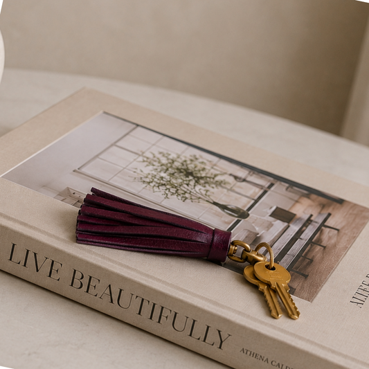 Llavero de cuero violeta con flecos y herraje vintage sobre libro decorativo beige estilo luxury